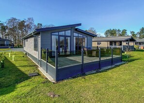 A modern house with a glass enclosure, a fenced deck, and a well-maintained lawn.