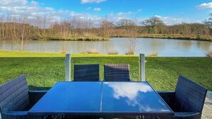 A table and chairs with a view of a lake and trees. - Lakeside 14 Casa Pet Friendly (Woodhall Spa)