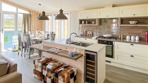 A modern kitchen with a central island, pendant lighting, and a view to the outside. - Lakeside 14 Casa Pet Friendly (Woodhall Spa)