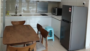 A modern kitchen with white cabinets, a stainless steel refrigerator, a microwave, and a dining area with a wooden table and chairs. - Suasana Damai (Petaling Jaya)