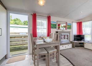 Um quarto com uma mesa de jantar, cadeiras, lareira, televisão e uma porta de vidro corrediça para o exterior.