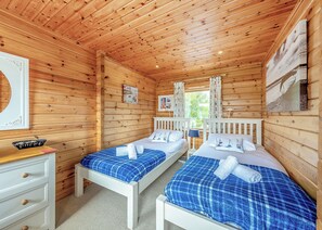 Una cabaña de madera con dos camas, un aparador y una ventana con cortinas.