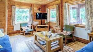 A cozy cabin interior with wooden walls, a television, a dining table, and two green chairs.
