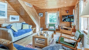 A cozy cabin interior with a wooden staircase, a sofa, a chair, a coffee table, and a television.