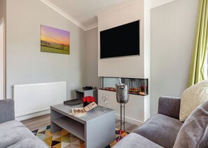 A modern living room with a flat-screen TV, a coffee table with red roses, a radiator, and a colorful rug.