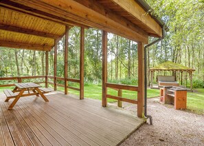 A covered wooden deck with picnic tables, a barbecue grill, and a gazebo in a forested area. - 2 bedroom accommodation in Freehay, Cheadle (Freehay, Cheadle)