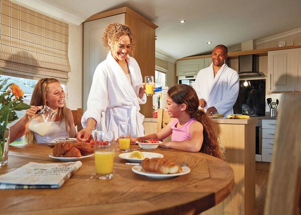 Café da manhã em família em cozinha moderna, com armários de madeira, mesa de jantar e vista para o exterior.