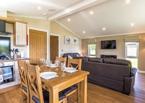 Uma sala de estar moderna com uma mesa de jantar de madeira posta para quatro pessoas, um sofá de couro escuro e uma televisão de tela plana fixada na parede.