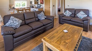 A modern living room with two brown leather sofas, a wooden coffee table, and a kitchen in the background.