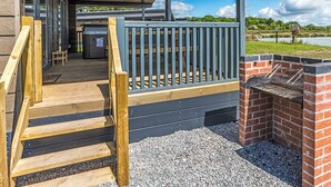A covered outdoor area with a wooden staircase, a grill, and a view of a lake.