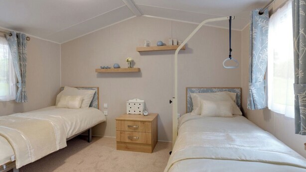 A bedroom with two single beds, a bedside table with a lamp, and a shelf above the door.