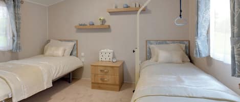 Un dormitorio con dos camas individuales, una mesita de noche con lámpara y un estante sobre la puerta.