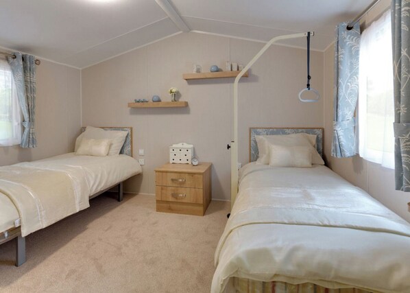 Une chambre avec deux lits simples, une table de chevet avec une lampe et une étagère au-dessus de la porte.