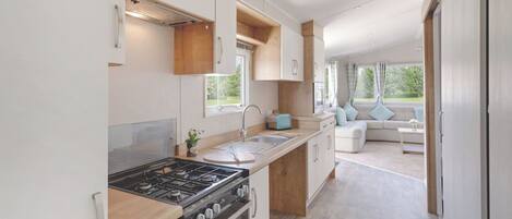 Et moderne camper-køkken med komfur, ovn og vask, der fører til en opholdsstue med sofa og vinduer.