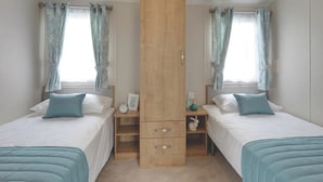 A bedroom with two beds, a wooden wardrobe, a nightstand, and a window with curtains.