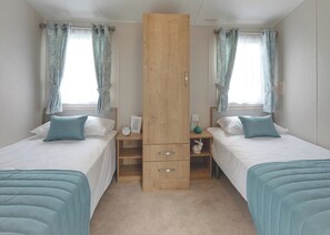 A bedroom with two beds, a wooden wardrobe, a nightstand, and a window with curtains.