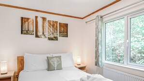 A bedroom with a bed, a nightstand with a lamp, a window with a view of trees, and three wall-mounted paintings. - 2 bedroom accommodation in Freehay, Cheadle (Freehay, Cheadle)