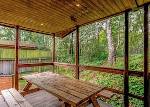 Um deck de madeira com uma mesa de piquenique, cercado por uma vedação de madeira e árvores.