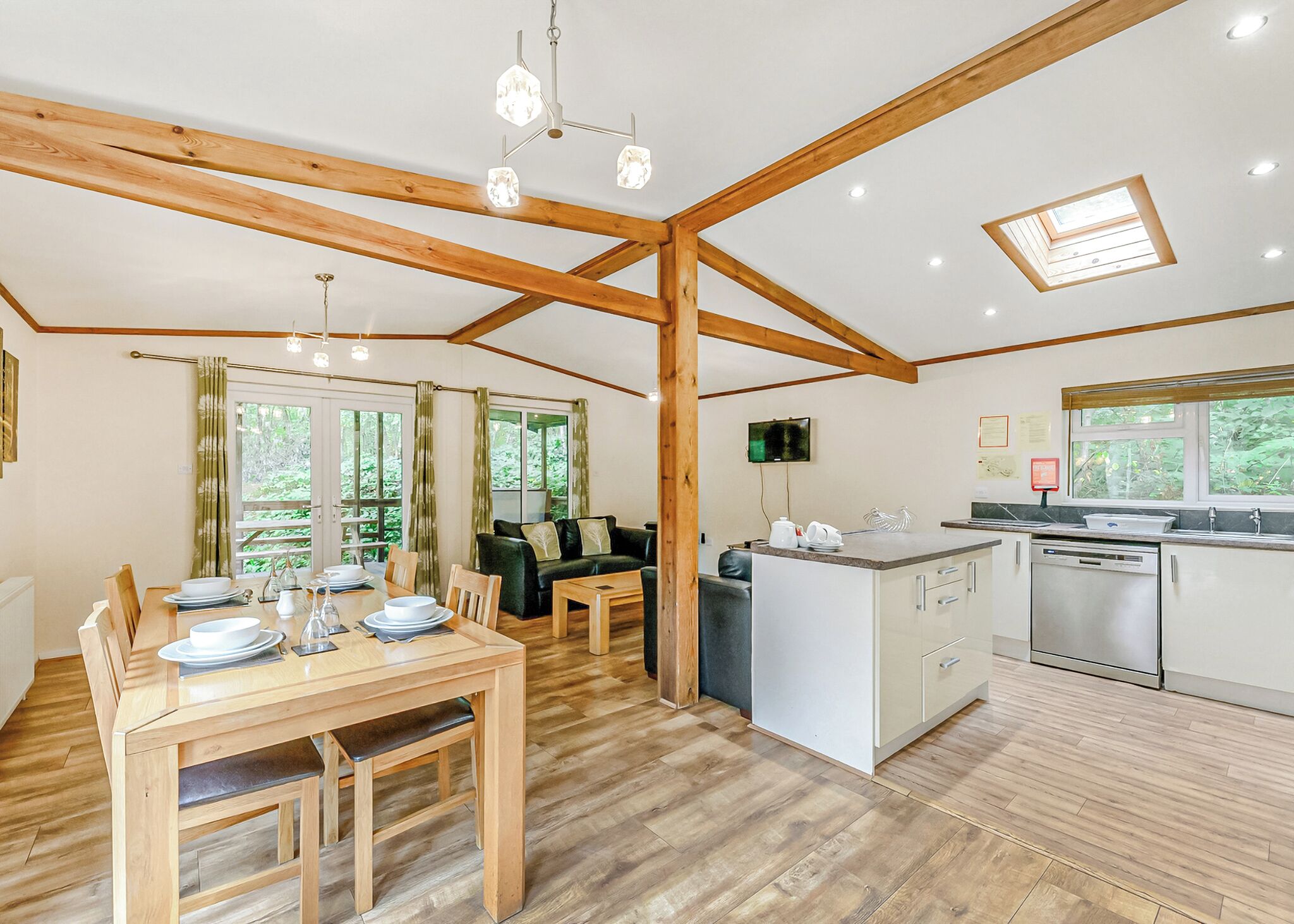 Une pièce spacieuse comprenant une table à manger en bois, un canapé, un coin cuisine avec un lave-vaisselle, ainsi qu’un plafond avec des poutres apparentes et des lucarnes.