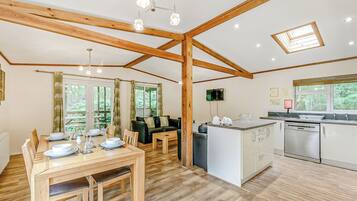Une pièce spacieuse comprenant une table à manger en bois, un canapé, un coin cuisine avec un lave-vaisselle, ainsi qu’un plafond avec des poutres apparentes et des lucarnes.