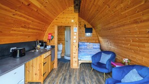 L’intérieur d’un chalet accueillant comprend une cuisine, une salle de bain et un coin salon avec des chaises bleues.