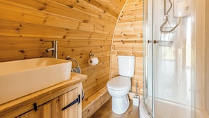Une salle de bain rustique, aménagée dans une cabane en bois, avec un lavabo, des toilettes et une douche fermée par des parois de verre.