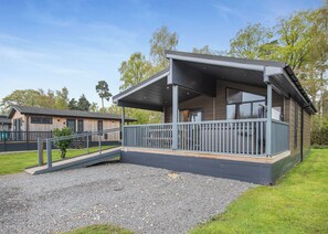 A modern building with a covered outdoor area, a wooden deck, and a gravel path leading to the entrance.