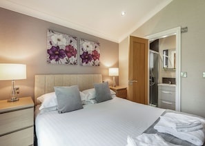 Une chambre d’hôtel avec un lit, deux tables de chevet, une porte en bois, un miroir dans la salle de bain et une serviette sur le sol.