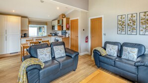 A living room with a sofa set, a dining table, and a kitchen area with cabinets and a microwave. - 2 bedroom accommodation in Woodhall Spa (Woodhall Spa)