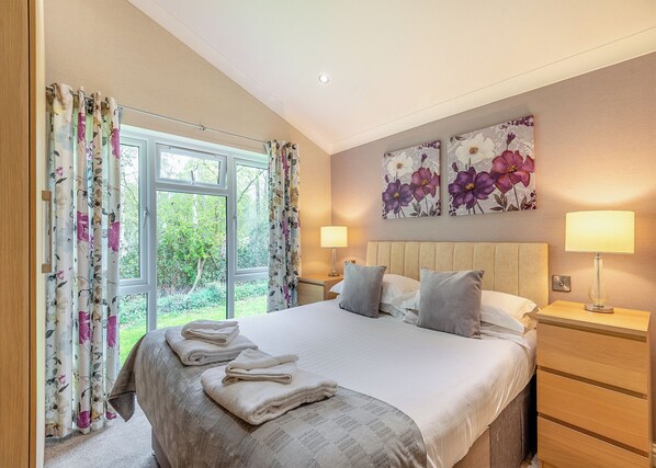 Ein Schlafzimmer mit einem großen Bett, zwei Nachttischlampen, einem Fenster mit Vorhängen und floralen Bildern an der Wand.