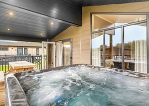 Un espace avec un bain à remous, une terrasse en bois, des portes vitrées et une vue sur l’extérieur.