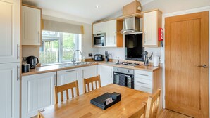 A modern kitchen with white cabinets, a wooden dining table, and a view of the outdoors. - 2 bedroom accommodation in Woodhall Spa (Woodhall Spa)