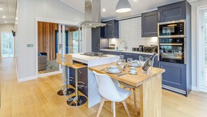 A modern kitchen with a central island, built-in appliances, and a dining area with bar stools. - 1 bedroom accommodation in Haddon (Haddon)