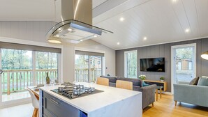 A modern kitchen with a central island, a dining area with a table and chairs, a living room with a sofa and TV, and large windows with a view of the outdoors. - 1 bedroom accommodation in Haddon (Haddon)