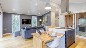 A modern kitchen with a central island, a dining area with a wooden table, and a living room with a sofa and TV. - 1 bedroom accommodation in Haddon (Haddon)