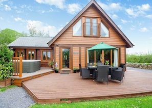 A wooden cabin with a deck, a hot tub, and outdoor seating. - Spacious, light, all wood luxury lodge in tranquil location at head of lake. (Anglesey)