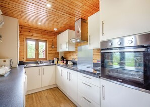 Une cuisine moderne avec un plafond en bois, des armoires blanches, des appareils électroménagers en acier inoxydable et une fenêtre donnant sur un paysage verdoyant.