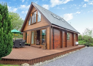 A wooden cabin with a deck, large windows, and a covered outdoor seating area. - Spacious, light, all wood luxury lodge in tranquil location at head of lake. (Anglesey)