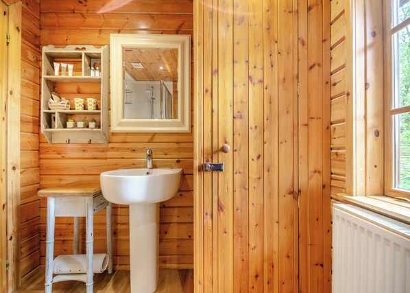 A wooden-paneled bathroom with a white sink, a mirror, and shelves with toiletries.