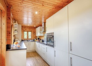A modern kitchen with wooden ceiling, white cabinets, stainless steel appliances, and a window. - Spacious, light, all wood luxury lodge in tranquil location at head of lake. (Anglesey)