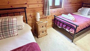 Une chambre dans un chalet en bois, avec deux lits, une table de chevet et une fenêtre avec des rideaux.