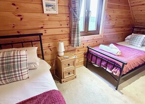 Une chambre dans un chalet en bois, avec deux lits, une table de chevet et une fenêtre avec des rideaux.