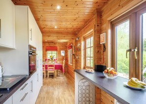 A wooden cabin kitchen with a dining area, wooden ceiling, and large windows.