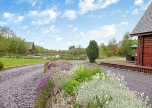 Un jardin avec un chemin de gravier, une terrasse en bois et un bâtiment doté d’un toit en pente.