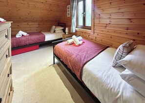 Une chambre de style cabane avec deux lits simples, une commode en bois et une fenêtre avec des rideaux.