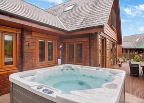 Une cabane en bois dotée d’un bain à remous, d’une terrasse en bois et d’un petit espace salon extérieur.