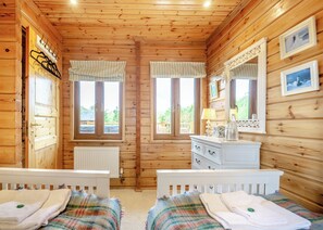 Une pièce de style cabane en bois, avec deux lits, une commode, un miroir et des fenêtres.