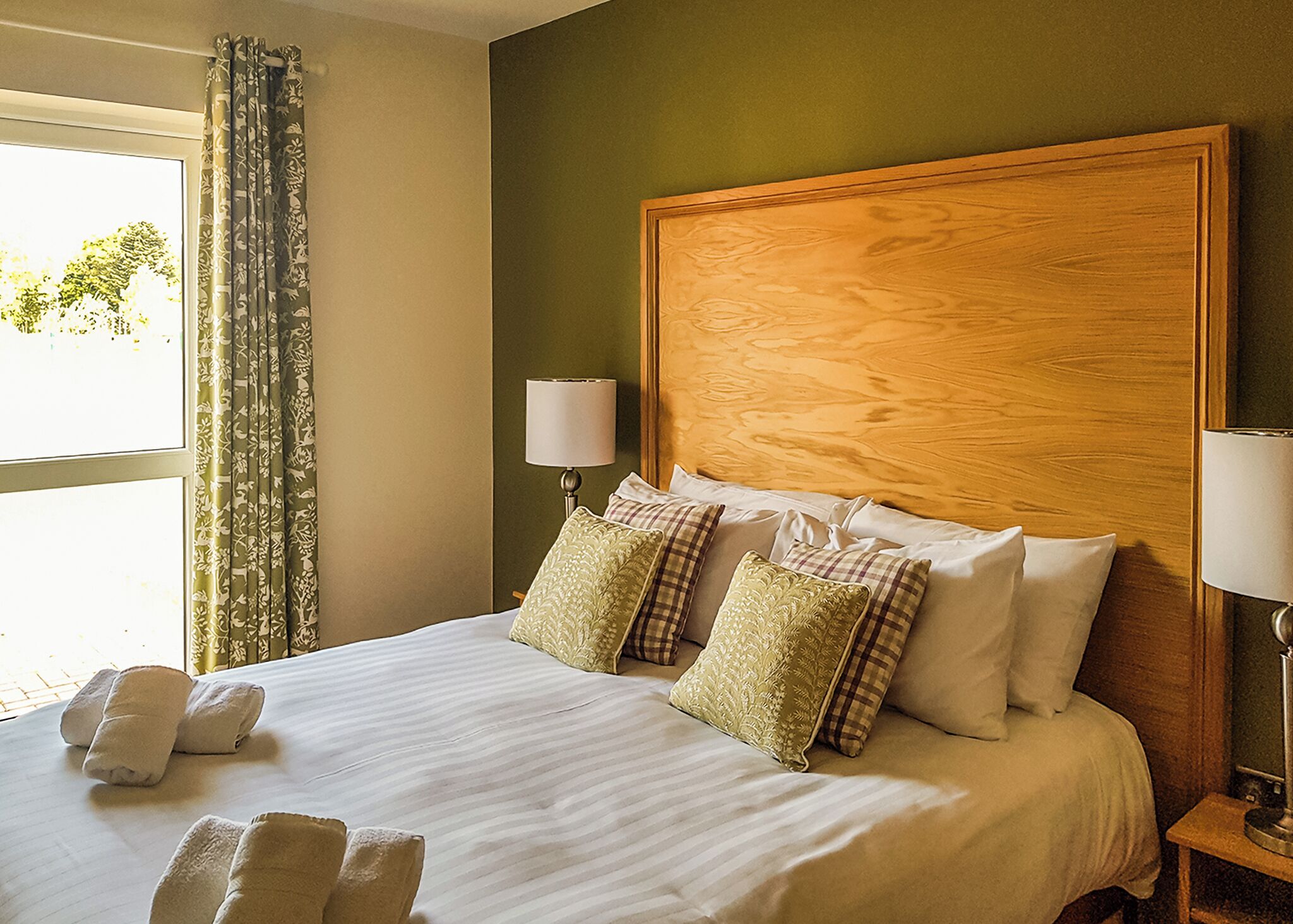 Habitación de hotel con una cama grande, dos lámparas de noche y un ventanal con cortinas.