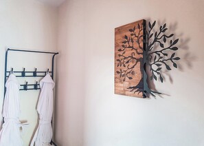 A room with a wall-mounted towel rack holding two towels, a wooden wall art piece with a tree design, and a plain wall.