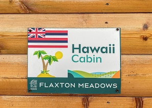 En skylt med texten ”Hawaii Cabin” vid ”Flaxton Meadows”, med en brittisk flagga, palmer och en sol.
